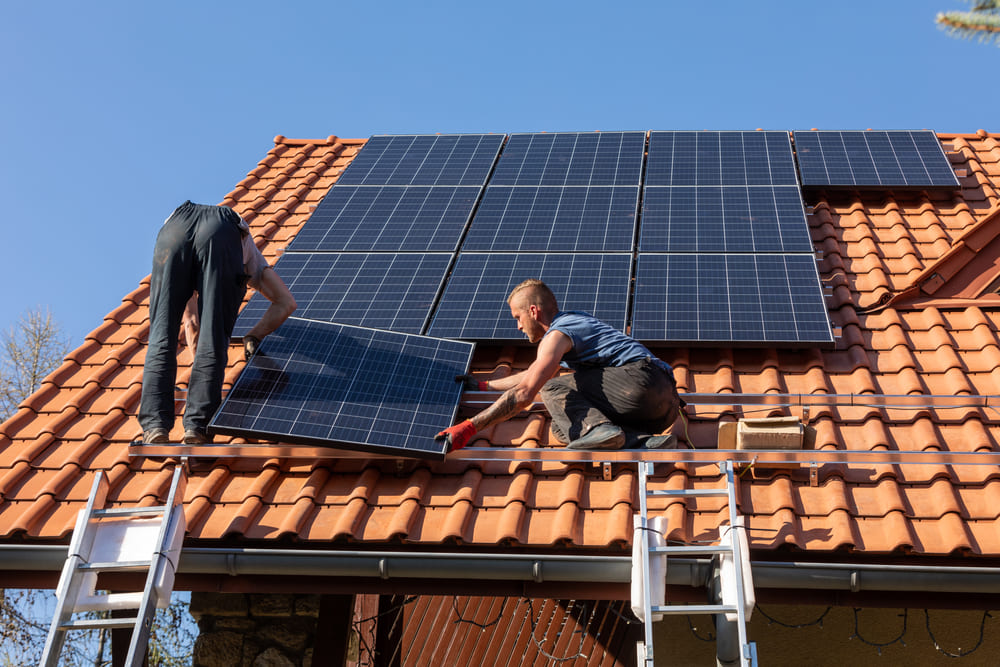 Deux électriciens posent des panneaux solaires sur un toit de maison