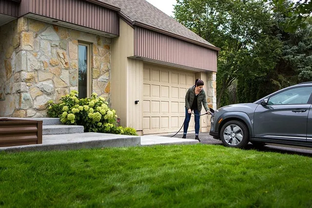 femme rechargeant son véhicule électrique devant sa maison